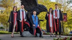 身穿毕业礼服的波沃罗五胞胎站在一座巨大的红鹰雕像前.